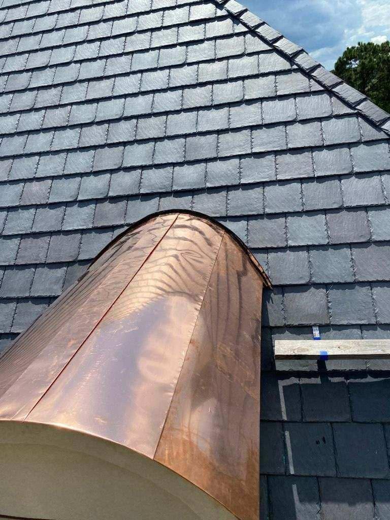 Close-up of curved copper roof work meeting textured gray roof courses